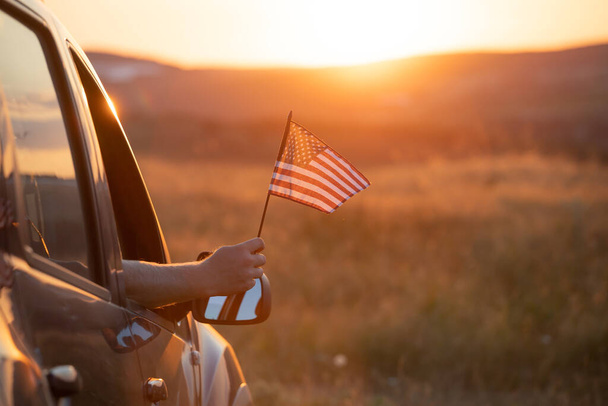 Man holding an American flag on a road trip. Independence Day or traveling in America concept. - 写真・画像