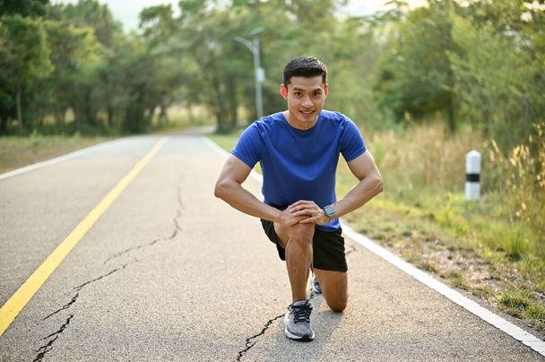 Happy millennial Asian man in sportswear is on the street in a nature park with a starting position. Leisure and lifestyle concept - Foto, Imagen