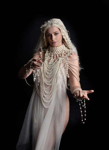 Retrato de cerca de la hermosa modelo rubia que lleva un vestido de perla extravagante joya. Brazos gestacionales extendiéndose, aislados sobre un fondo negro de estudio. - Foto, Imagen