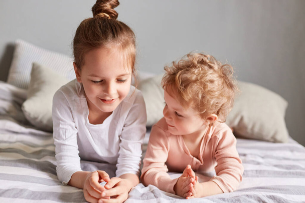 Sisters lying on bed in bedroom playing together relaxing in the morning talking having fun, caucasian kids at home in bedroom, wearing casual clothing. - Fotoğraf, Görsel