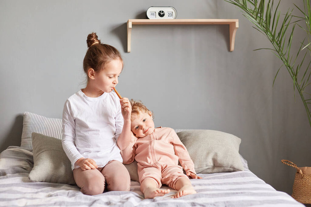 Cute adorable little children in casual outfits sitting on bed in their bedroom with toothbrushes, taking care of their oral hygiene in the morning. - Valokuva, kuva