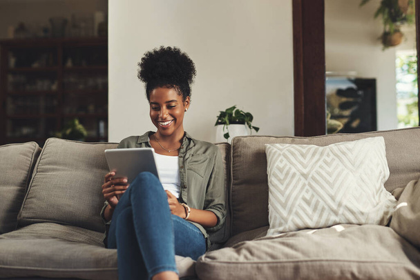 Fühlen Sie sich gemütlich und wohl zu Hause. eine schöne junge Frau, die ein digitales Tablet benutzt, während sie es sich zu Hause auf ihrem Sofa gemütlich macht - Foto, Bild