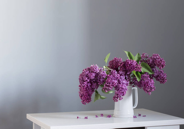 beautiful lilac flowers in white jug on white wooden table - Fotó, kép