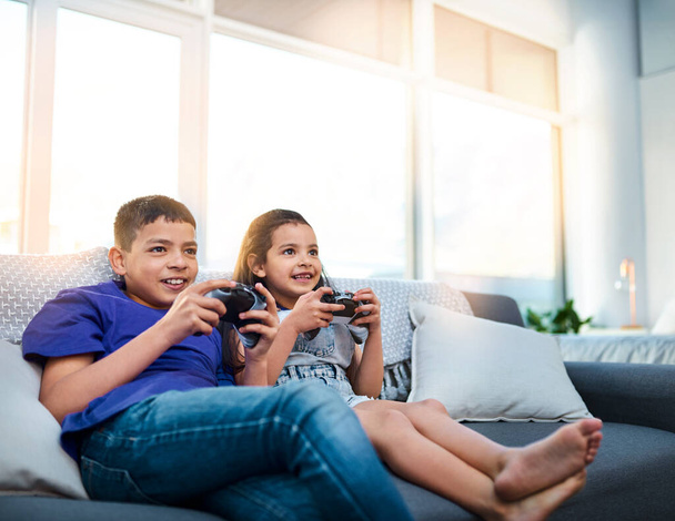 Were always competitive when we play against each other. two young children sitting on a sofa and playing video game at home - Fotografie, Obrázek