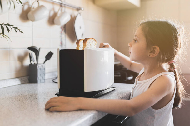 5 - 7 year old kid girl who is preparing breakfast from toast in a toaster in cozy home interior, selective soft focus. - Φωτογραφία, εικόνα