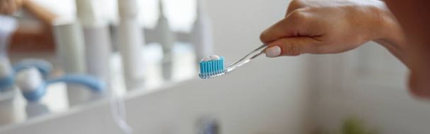 Close up of blue toothpaste on toothbrush in hand of Caucasian woman. Cleaning teeth. Morning time. - Foto, immagini