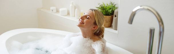 Happy cheerful pretty female enjoying bubbles and hot water in bathtub. Spa and relax day. Top view. - Foto, Bild