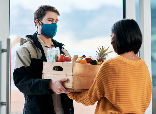Dobrá bezpečnostní opatření ukazují dobrou profesionalitu. maskovaný mladý muž donáší čerstvé ovoce a zeleninu ženě doma - Fotografie, Obrázek