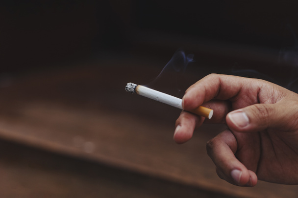 Чоловік тримає палити цигарку в руці
 - Фото, зображення