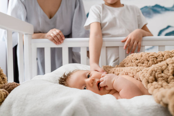 Portret noworodka z ukochaną sylwetką dłoni rodzinnych na tle, dziecko leżało w łóżeczku w dziecięcej sypialni - Zdjęcie, obraz