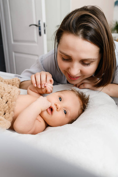 Hymyilevä nuori äiti pitää kädestä annetun vastasyntyneen vauvan vauvansängyssä kehdossa viihtyisässä kodin sisustuksessa, perheen rakkaudessa. - Valokuva, kuva