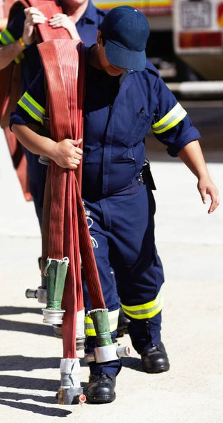 Firefighter, team and carrying hoses for emergency, rescue or fire drill from truck outdoors. Firefighters working together in practice lifting big liquid pressure pipes outside station or department. - Foto, Bild