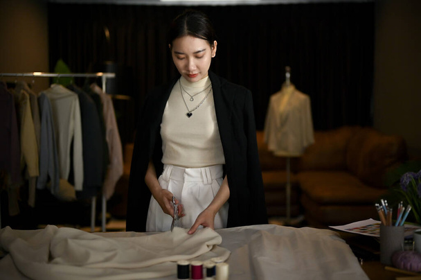 Професійна азіатська художниця, або дизайнер моди, використовує ножиці, щоб розрізати тканину, виготовляє візерунок тканини, працюючи в своїй студії. - Фото, зображення