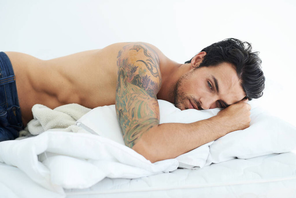 Sad, young man in bed and depressed in bedroom in white background. Sleeping for mental health, insomnia and shirtless male person resting for peace or comfort on mattress in studio backdrop. - Foto, immagini