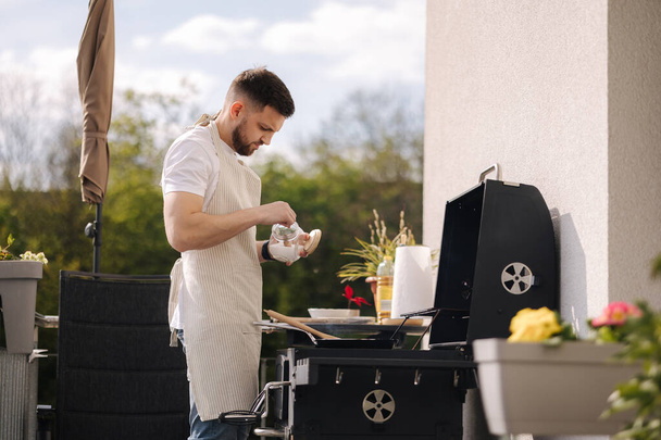 Homme nourriture salée dans la poêle et préparer le repas en plein air sur barbecue grill. Photo de haute qualité - Photo, image
