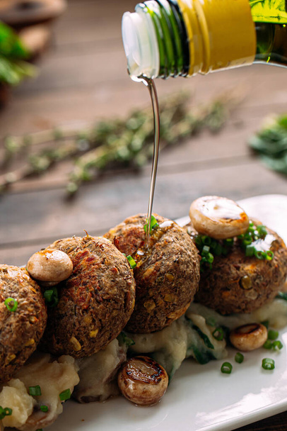 Olivenöl auf Falafeln mit Pilzen und Kartoffelpüree gießen - Foto, Bild