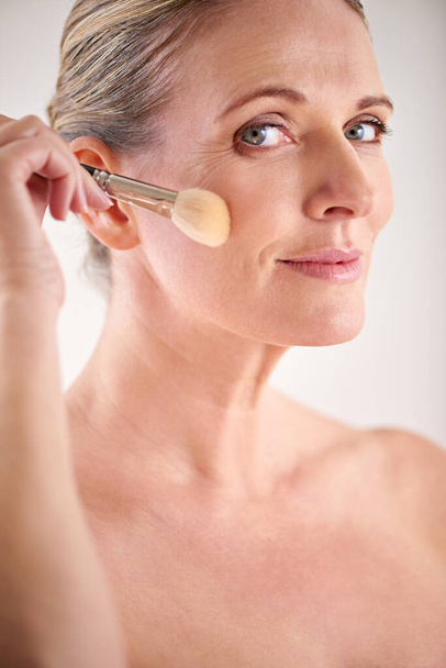 Adding a touch of blush. Cropped studio shot of an attractive mature woman applying makeup with a brush - Fotó, kép