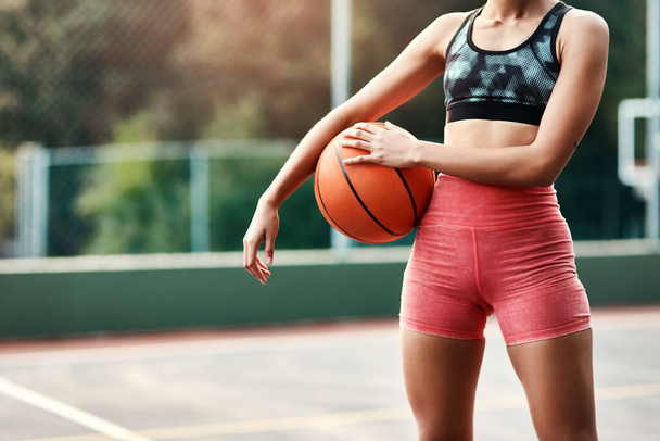 Είμαι στο σπίτι μου στο γήπεδο. μια αγνώριστη αθλήτρια που στέκεται μόνη της στο γήπεδο και κρατά μια μπάλα μπάσκετ κατά τη διάρκεια της ημέρας. - Φωτογραφία, εικόνα