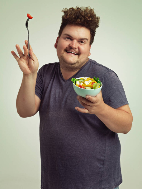 The salad dance. Studio shot of an overweight man holding a bowl of salad in a silly pose - Photo, Image