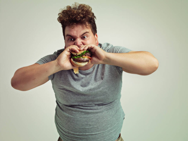これは今までで最高のバーガーです。スタジオショットの太りすぎの男のハンバーガーにかむ - 写真・画像