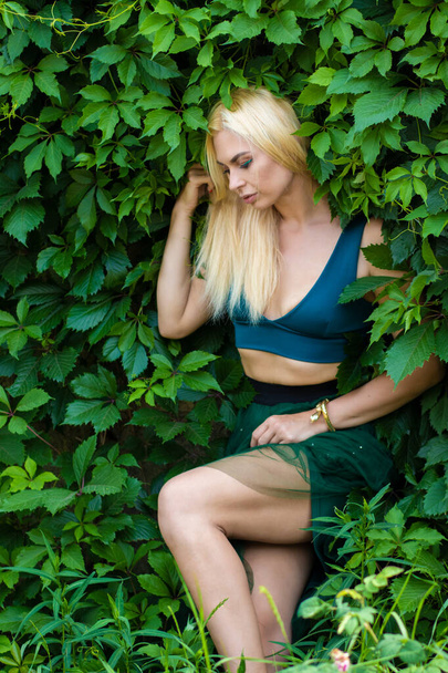 Mooi fashion blond model genieten van de natuur, ademen frisse lucht in de zomertuin over groene bladeren achtergrond. Harmonieconcept - Foto, afbeelding