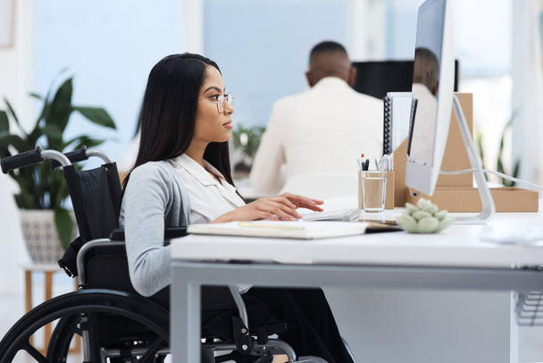 Skupiony na zadaniu. atrakcyjna młoda bizneswoman na wózku inwalidzkim pracująca przy biurku w biurze - Zdjęcie, obraz