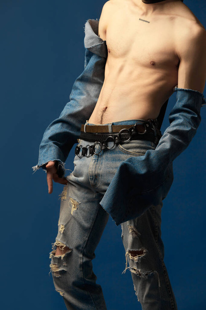 Cropped image of young man posing shirtless in jeans clothes against blue studio background. Vibe of hippie. Relief body. Concept of mens fashion, extraordinary style, art, beauty, trends - Foto, Imagem