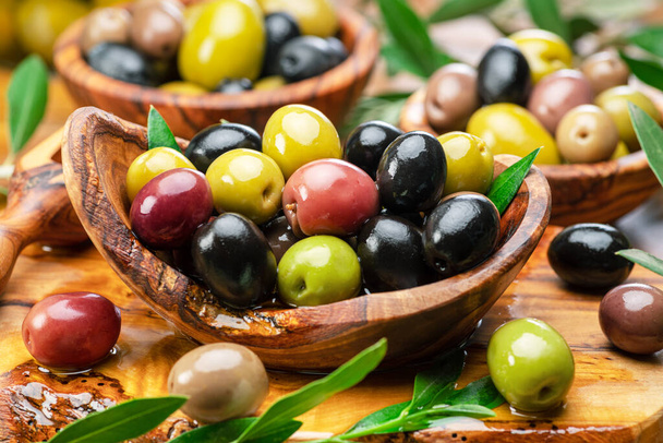Kalamata, green and black olives in the wooden plate. Food background. - Фото, изображение