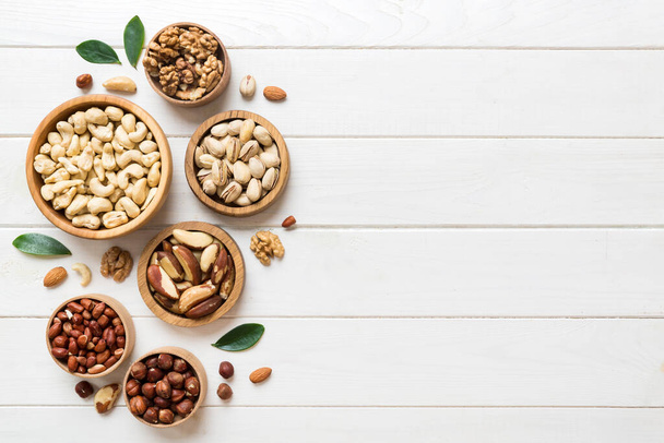 mixed nuts in wooden bowl. Mix of various nuts on colored background. pistachios, cashews, walnuts, hazelnuts, peanuts and brazil nuts. - Foto, Imagen