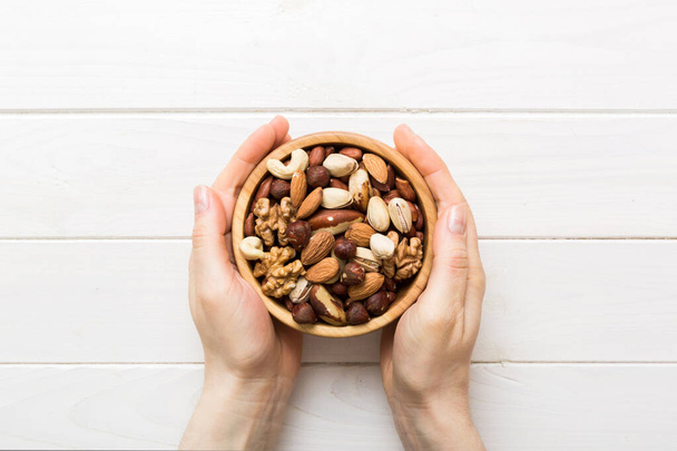 Vrouw handen met een houten kom met gemengde noten Walnoot, pistachenoten, amandelen, hazelnoten en cashewnoten. Gezond eten en eten. Vegetarische snacks van verschillende noten. - Foto, afbeelding