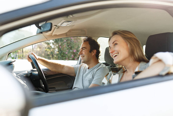 Emocional pareja milenaria divirtiéndose mientras viaje en coche, escuchando música y cantando alegremente, disparado desde el interior del auto, resplandor solar. - Foto, imagen