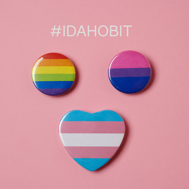 duhové, bisexuální a transgenderové vlajky na růžovém pozadí a hashtag IDAHOBIT, stojící na mezinárodní den proti homofobii, bifobii a tranfobii - Fotografie, Obrázek