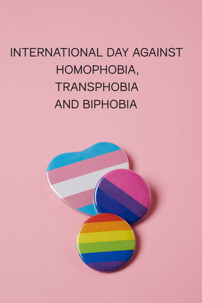текст международного дня борьбы с гомофобией, трансфобией и бифобией, а также несколько значков с флагом гей-прайда, флагом транссексуального прайда и флагом бисексуального прайда на розовом фоне - Фото, изображение