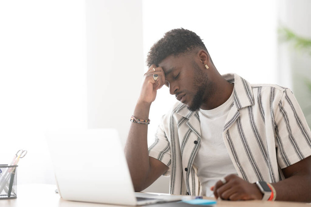 Разочарованный чёрный мужчина перед ноутбуком. Концепция стресса и депрессии. - Фото, изображение