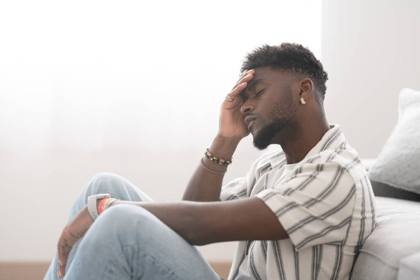 Üzgün ve endişeli Afrikalı Amerikalı genç adam yerde oturuyor. Depresyon, üzüntü ve stres konsepti. - Fotoğraf, Görsel