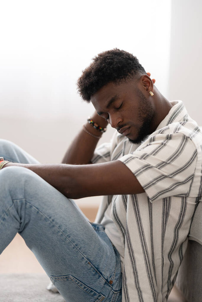 アフリカ系アメリカ人の悲しい男が床に座って考えている。うつ病を患っている黒人. - 写真・画像