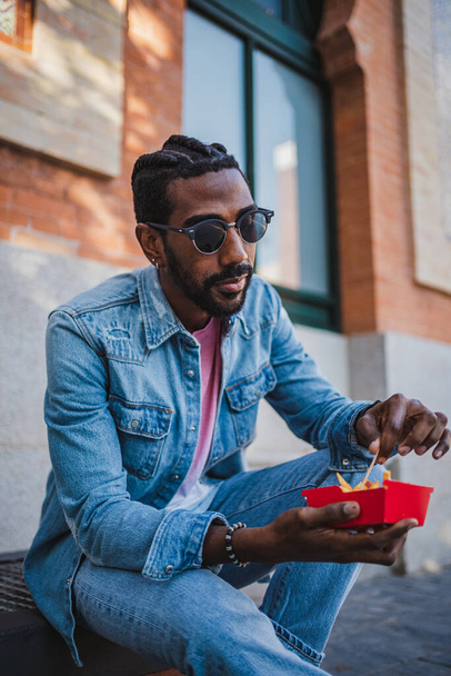 Jongeman die fastfood eet op straat terwijl hij even pauze neemt van zijn werk. - Foto, afbeelding