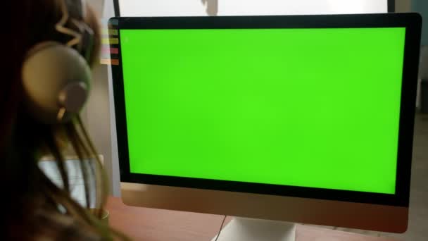 Vista recortada de uma mulher com auscultadores a trabalhar num computador. Uma jovem senta-se em frente a um monitor com uma tela verde. Imagens 4k de alta qualidade - Filmagem, Vídeo