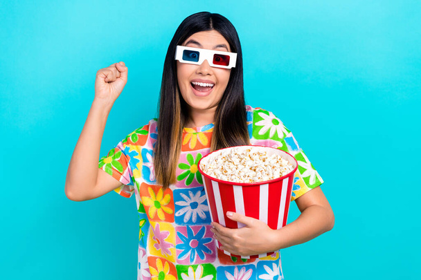 Photo of funky lucky woman dressed flower print t-shirt rising fist eat pop corn watching vr film isolated blue color background. - 写真・画像