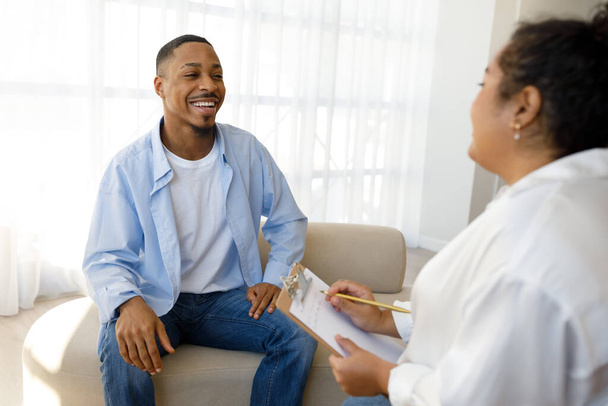 Mental health, psychological support, help concept. Cheerful handsome millennial african american guy smiling to young woman psychotherapist at clinic, thankful for successful session - Zdjęcie, obraz