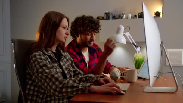 Twee jongeren zitten achter een computer en praten over iets. Een man met krullend haar helpt zijn collega een video te bewerken. Hoge kwaliteit 4k beeldmateriaal - Video