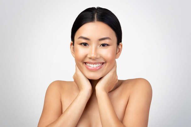 Bodycare And Wellbeing. Portrait Of Cheerful Japanese Woman Touching And Massaging Neck, Smiling To Camera Posing Shirtless Over Gray Background. Beauty And Pampering Routine. Studio Shot - Photo, image