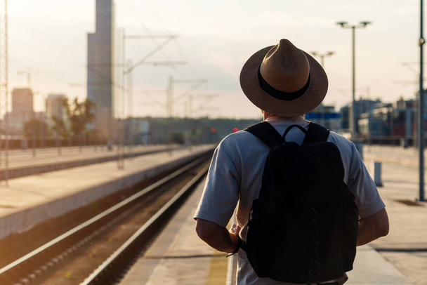 Turista vestido con sombrero de paja de pie en la plataforma ferroviaria y tren de espera. - Foto, imagen