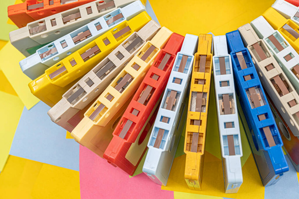 Vista superior de una colección de casetes de cinta de audio retro antiguos multicolores con un fondo de notas adhesivas de papel multicolor - Foto, Imagen