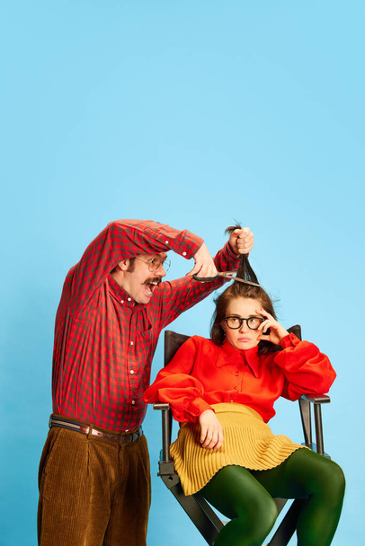 Bad service. Portrait with sad, upset woman, client and crazy barber, female hairdresser doing new haircut over blue background. Concept of barbershop, new style, beauty, fashion, human emotions, ad - Zdjęcie, obraz