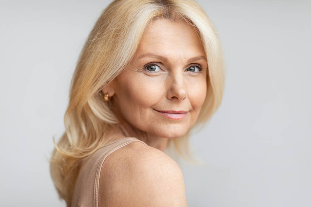 Portrait of happy senior woman with flawless skin and natural makeup posing on light background, free space. Beautiful good-looking aged lady - Фото, изображение