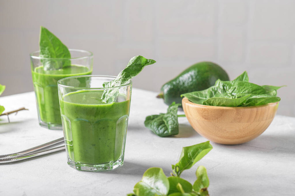 Gezonde groene smoothie met spinazie, avocado, banaan en veganistische melk in twee glazen en verse ingrediënten op lichtgrijze tafelachtergrond. Detox, dieet, gezond, vegetarisch voedselconcept - Foto, afbeelding