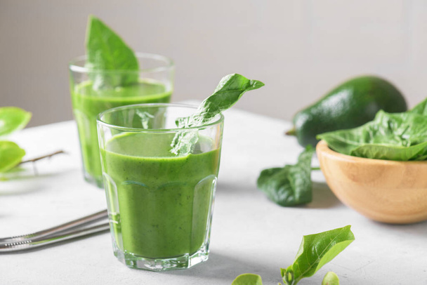 Zdrowy zielony smoothie ze szpinakiem, awokado, banan i mleko wegańskie w dwóch szklankach i świeżych składników na jasnoszary stół tle. Detox, dieta, zdrowe, wegetariańska koncepcja żywności - Zdjęcie, obraz