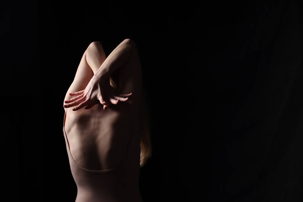 Ballerina in a beige bodysuit. Dark background. Sculpted beautiful female body. Pose of a gymnast. - Φωτογραφία, εικόνα