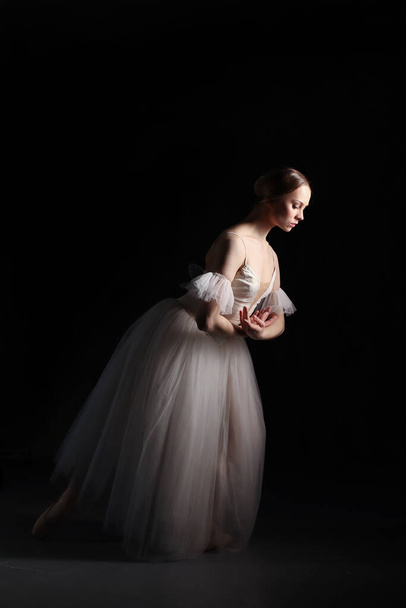 Professional ballerina dancing ballet.Ballerina in a white dress and pointe shoes. Dark background. Beautiful female body. - Zdjęcie, obraz